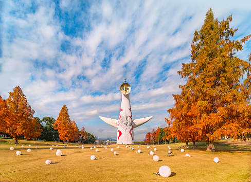 japan, osaka - dec 04 2022: The Japanese Tower of the Sun or taiyou no tou created by Taro Okamoto for Expo '70 towering 70 meters above the dried lawn and conifers browned by the autumn season.