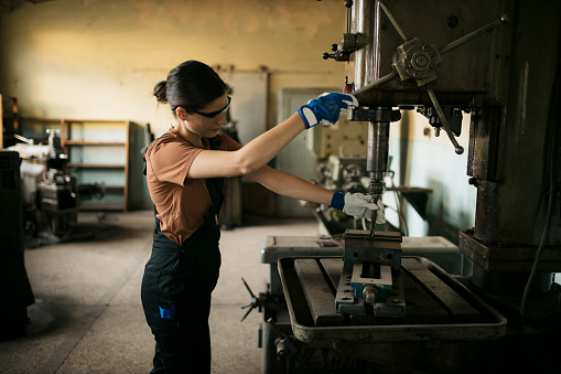 Female operator working in a metal working industry installing a dill bit on drill press. Woman professional metalworker operating drilling machine in manufacturing workshop.