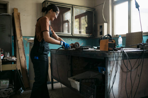 istock Woman employee in safety wear cutting a workpiece using angle grinder in meal workshop 1634605414