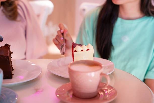 A young woman eating cakes with her beautiful grandma in a bakery while drinking some coffee