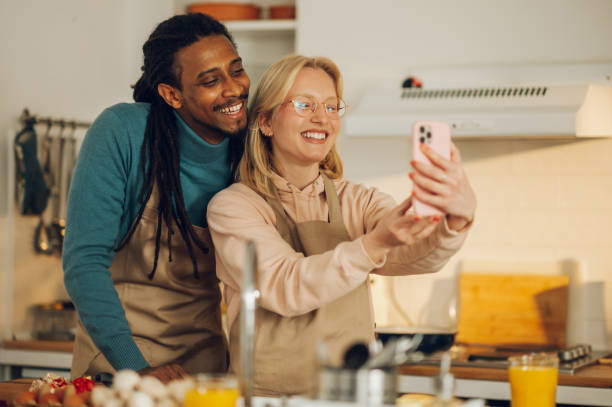 istock A happy multicultural couple is taking self-portraits in the kitchen while cooking dinner at home together. 1634689059