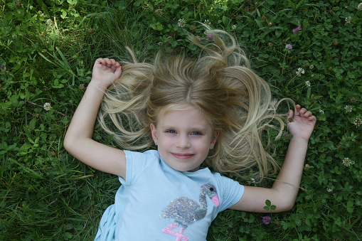 Adorable little girl with long blonde hair laying in the meadow, top view