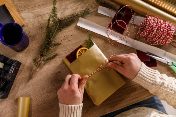 Young man wrapping and tying decorative twine around a Christmas gift box stock photo