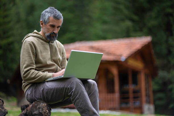 istock Cabin getaway. Man with laptop in log cabin. 1634740742