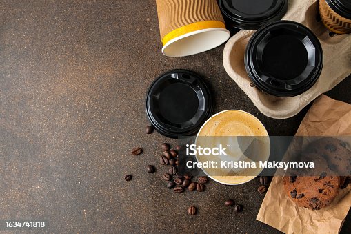 istock Paper cups with cappuccino on a stand, coffee beans and chocolate chip cookies on a brown table. coffee to go 1634741818
