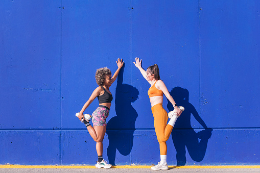 two sportswomen stretching together outdoors in a sunny day, concept of friendship in sport and active lifestyle, copy space for text