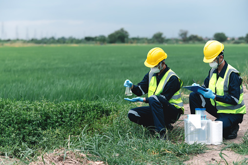 Two Environmental Engineers Inspect Water Quality and Take Water Samples Notes in The Field Near Farmland, Natural Water Sources maybe Contaminated by Toxic Waste with Copy Space.