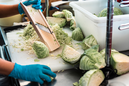 Still image of a restaurant worker's hand holding a grater amongst cut cabbages.