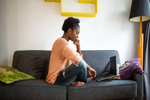 istock Side of serious young black woman sitting on sofa using laptop computer 1634747746
