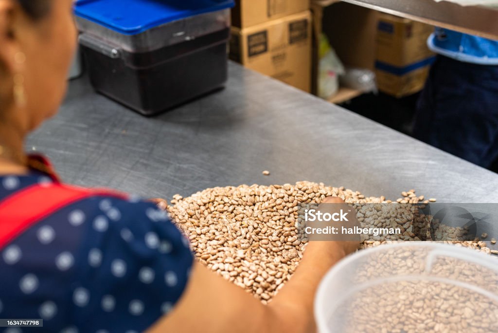 Over-the-shoulder Shot of Worker Sifting Through Peanuts A Hispanic woman sifting through peanuts in the kitchen of a Mexican restaurant during the day. 35-39 Years Stock Photo