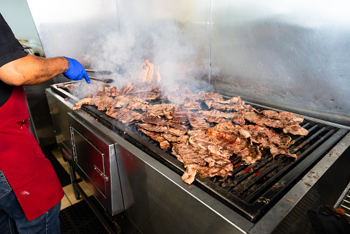 Multiple pieces of grilled meat sitting atop a charcoal grill inside a Mexican restaurant.