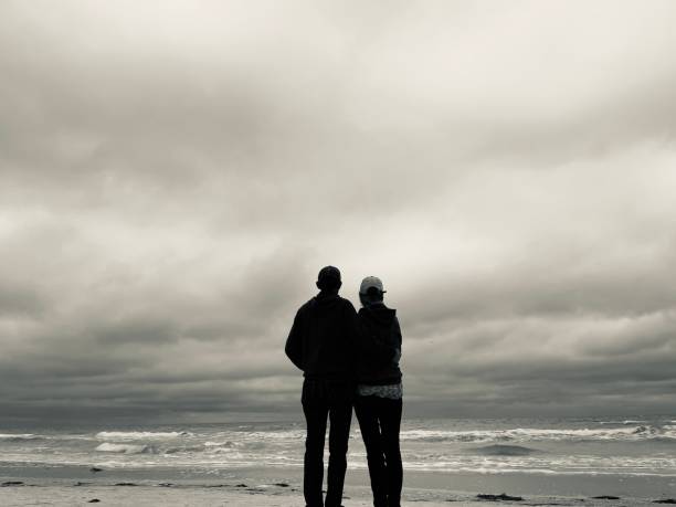 Uncertain future. Rear view of  senior couple standing on beach  as they look out over water and stormy skies.  Monochromatic on Indian Rocks Beach.