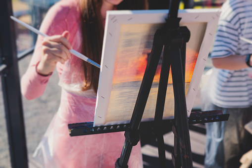Process of drawing, group class of talented students with painting easels and canvases during lesson of watercolour painting outdoors, drawing class for adult artists
