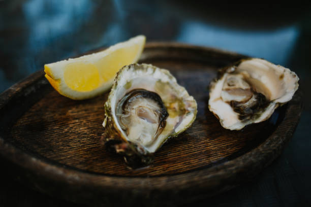 istock Two fresh oysters with lemon slice on a wooden plate in a fish restaurant. 1634854351