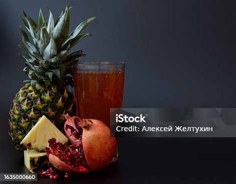 istock A glass of freshly squeezed juice on a black background and pieces of ripe pineapple and a broken pomegranate fruit with seeds. 1635000660