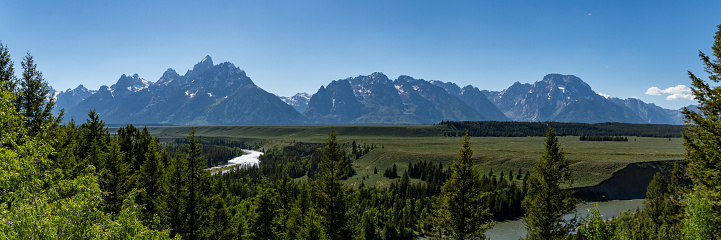 The snow capped mountian range of the Grand Teton National Park in Wyoming in the summer time with the green grass and blue skies