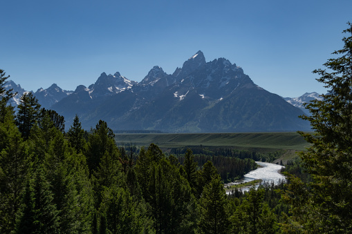 The snow capped mountian range of the Grand Teton National Park in Wyoming in the summer time with the green grass and blue skies