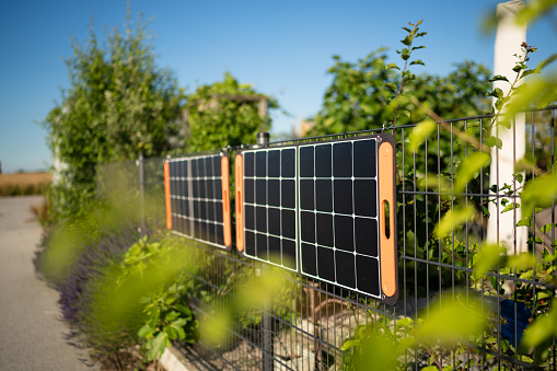 portable solar panels hanging on private garden fence on sunny day with blue sky to produce sustainable green energy