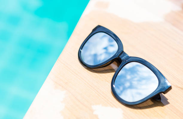 istock Closeup sunglasses with sky reflection on swimming pool edge with space on blue water background 1635131311