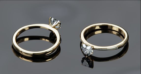 Two gold diamond rings sits on a shiny black glass surface. heart shaped diamond rings design with 3d rendering.