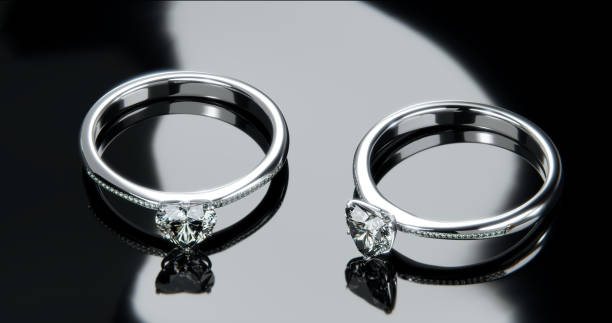 istock Two platinum diamond rings sits on a shiny black glass surface. heart shaped diamond rings design with 3d rendering. 1635145345