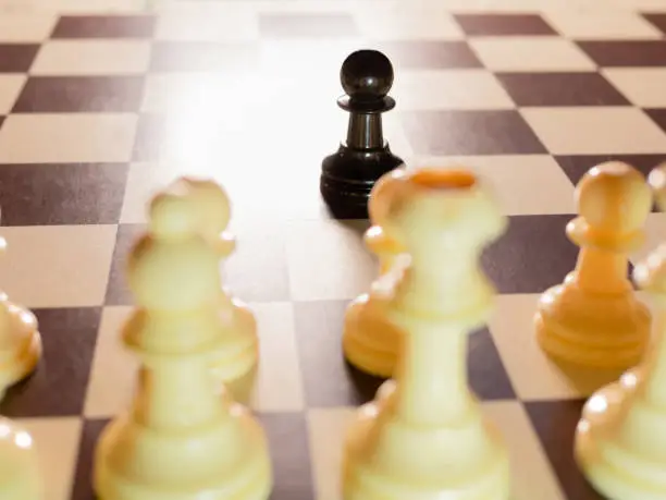 Black chess pawn against all white pieces. Concept of Racist Harassment. Selective focus
