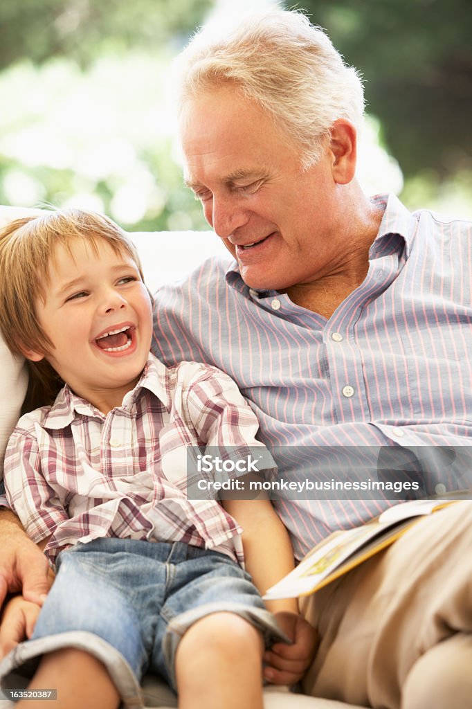 Grand-père et son petit-fils lire ensemble sur canapé - Photo de Grand-parent libre de droits