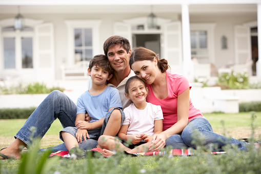 Family Sitting Outside House On Lawn Smiling Together