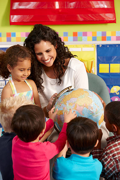 Elementary Age Schoolchildren In Geography Class With Teacher Group Of Elementary Age Schoolchildren In Geography Class With Teacher Looking At Globe preschool classroom jobs stock pictures, royalty-free photos & images