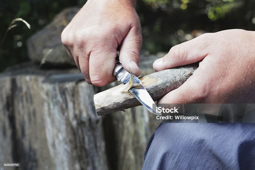 Man Carving Wooden Stick A man uses a bowie knife with a sharp blade to carve a wooden stick. Penknife Stock Photo