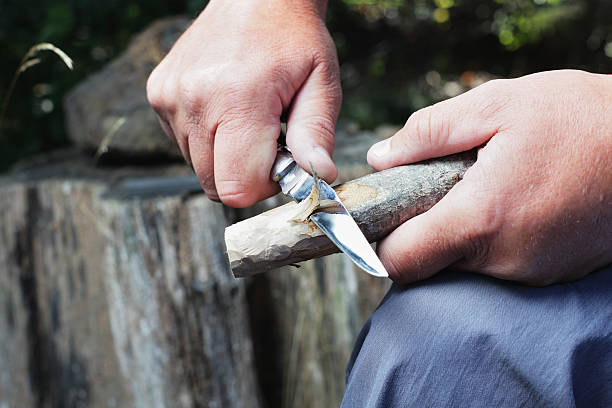 Man Carving Wooden Stick A man uses a bowie knife with a sharp blade to carve a wooden stick. penknife stock pictures, royalty-free photos & images