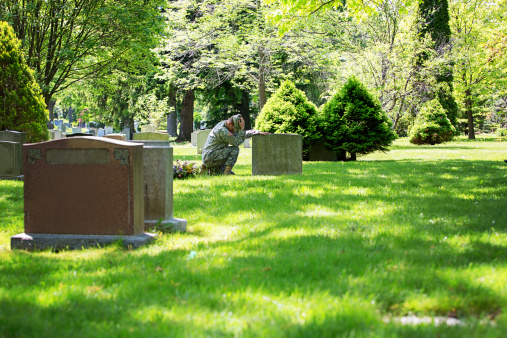 American vet kneeling at a grave in a cemetary to pay respect.