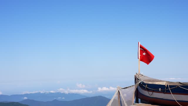 Turkish flag waving on the mountain top and wooden boat