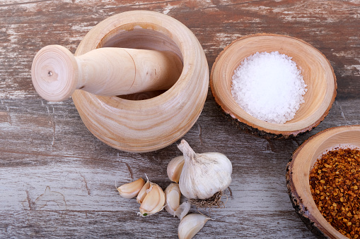 Ground dried garlic on a wooden spatula surrounded by whole heads of garlic