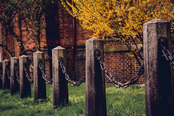 istock Old stone posts with chains on a background of green grass 1635272904