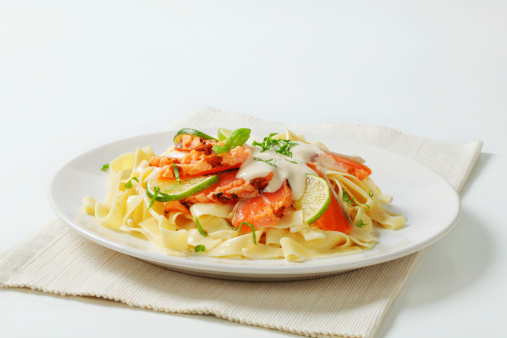 plate of freshly boiled pasta tagliatelle with salmon and lime slices in a light dressing on a white placemat