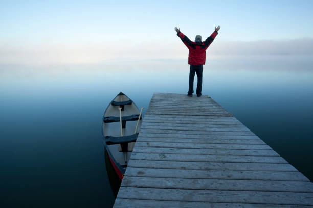 Riding Mountain National Park, Manitoba. Canoe at rest on a calm foggy day, with a person standing overlooking Lake Audy, Riding Mountain National Park, Manitoba.Canoe at rest on a calm foggy day, with a person standing overlooking Lake Audy, Riding Mountain National Park, Manitoba. riding mountain national park stock pictures, royalty-free photos & images