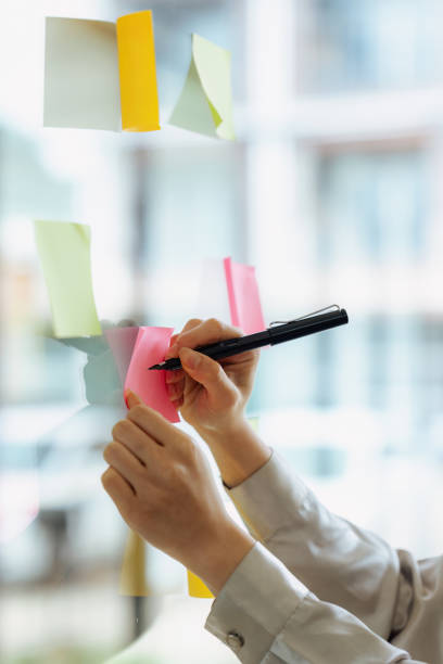 istock Through glass view of businesswoman analyzing process schedule, planning tasks on sticky papers 1635325022