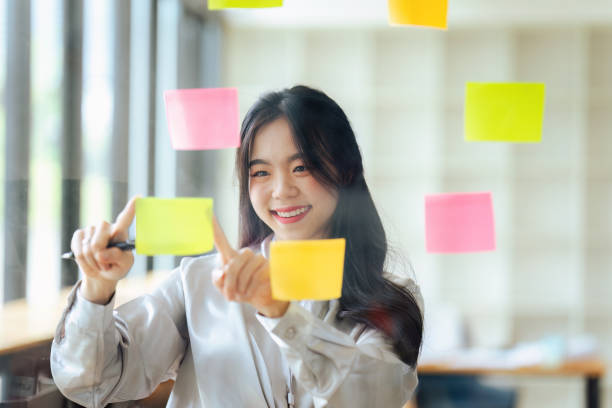 istock Through glass view of businesswoman analyzing process schedule, planning tasks on sticky papers 1635325270
