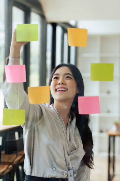 istock Through glass view of businesswoman analyzing process schedule, planning tasks on sticky papers 1635325552