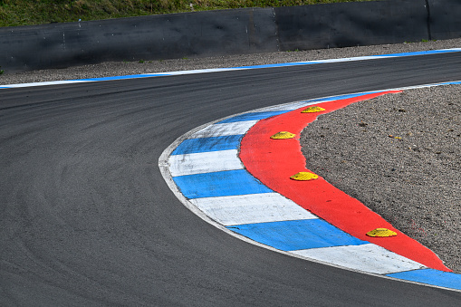 A vivid blue and chevron with a red inner semi circle and yellow safety caps depicting a corner on a tarmac race track, circuit, with rubber tyre marks imbedded on the track
