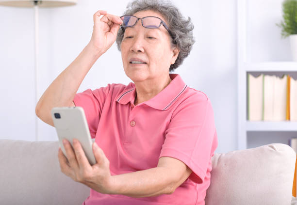 Presbyopia, senior asian woman holding eyeglasses having problem with vision problem trying to read text on mobile phone - fotografia de stock