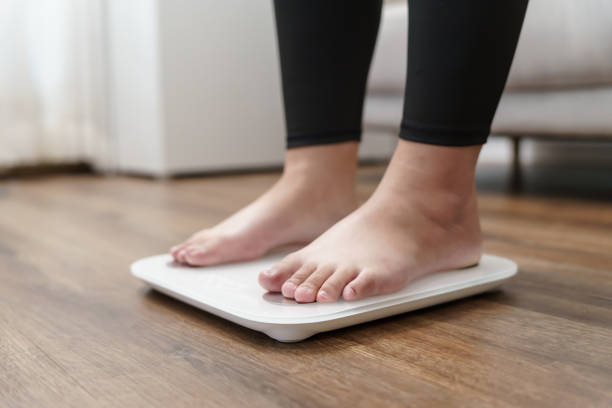 istock Fat diet and scale feet standing on electronic scales for weight control. Measurement instrument in kilogram for a diet control. 1635340334