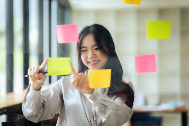 istock Through glass view of businesswoman analyzing process schedule, planning tasks on sticky papers 1635340471