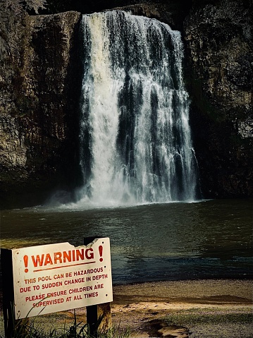 A caution sign in front of the stunning Hunua Falls waterfall