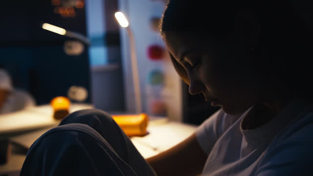 Worried Teenage Girl Sitting At Desk In Bedroom At Home Messaging On Mobile Phone At Night