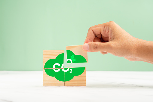 Wooden cubes with CO2 green icons over a marble floor against a green background. Renewable energy. Net-zero greenhouse gas emissions target. Green industries business and CO2 emission concept