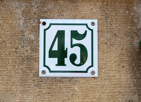 White metallic sign with black number digit 45 on rough brown plastered cement wall background. Signage bolted on stonewall.