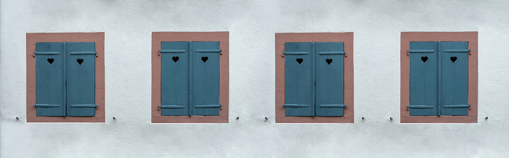 Windows with blue closed wooden shutters on white stone wall background. Shutter with heart hole, love symbol.