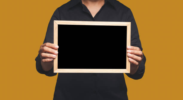 istock Close-up of hands holding a blank mini blackboard while standing on an orange background. Space for text 1635373527